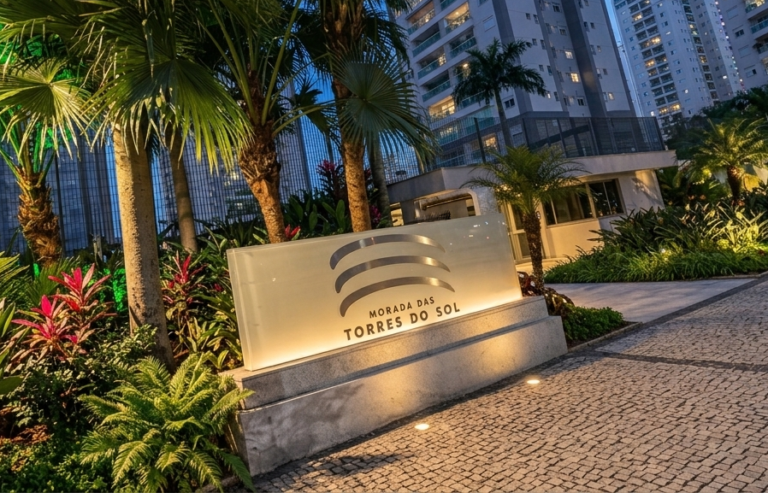 Totem iluminado de identificação de condomínio. Painel frontal em vidro de 6mm com jateamento, logótipo em letra caixa escura e iluminação interna na base, suportado por uma estrutura sólida.